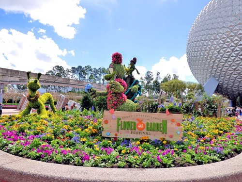 Colorful flower display at Epcot's Flower and Garden Festival, featuring topiary characters and a festival sign.