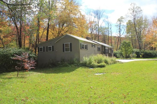 A cozy house surrounded by trees and colorful autumn foliage, set on a grassy lawn.
