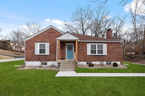 A charming brick house with a blue front door, surrounded by green grass and trees, on a clear day.