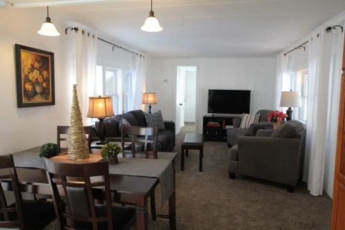 Cozy living room with gray furniture, a TV, and a dining area, featuring warm lighting and decorative plants.