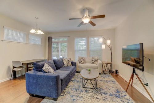Cozy living room with a blue sofa, coffee table, TV, and dining area, featuring natural light and modern decor.