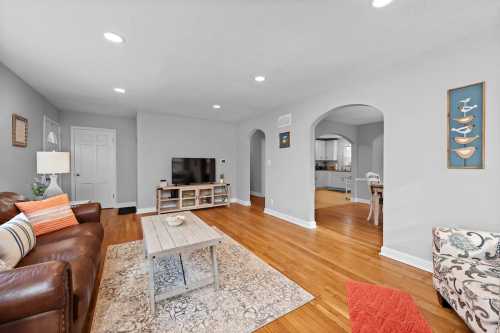 Cozy living room with a brown leather sofa, wooden coffee table, and light gray walls, leading to a kitchen area.