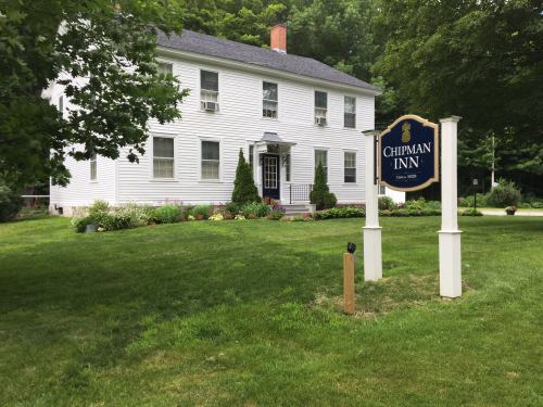 A white two-story inn with a sign reading "Chipman Inn," surrounded by green grass and trees.