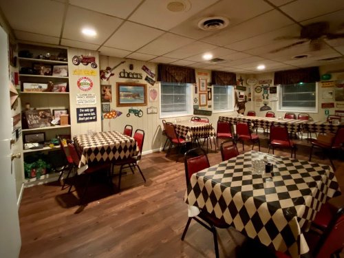 Cozy diner interior with checkered tablecloths, red chairs, and vintage decor on the walls. Warm, inviting atmosphere.