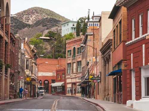 A quiet street lined with historic buildings, shops, and a mountain backdrop in a small town.