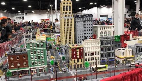 A detailed LEGO cityscape with buildings, streets, and miniature figures, set up at a crowded event.