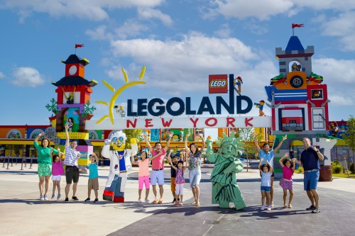 A group of people joyfully poses in front of the colorful LEGOLAND New York entrance with LEGO figures.