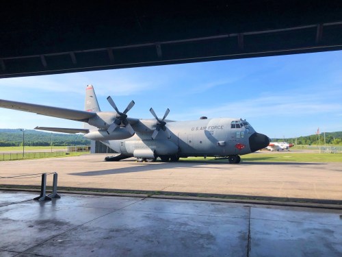 A U.S. Air Force C-130 aircraft parked on a tarmac, viewed from a hangar entrance.