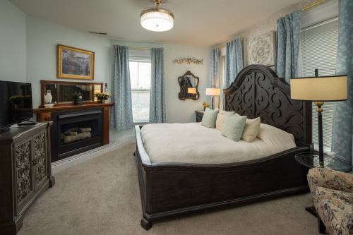 Cozy bedroom featuring a large bed, decorative fireplace, and elegant furnishings with soft blue accents.