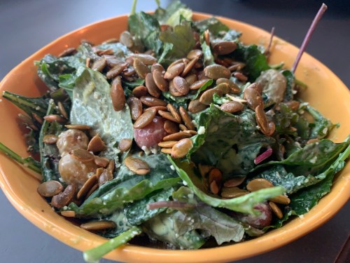 A vibrant salad in an orange bowl, featuring leafy greens, grapes, and topped with crunchy pumpkin seeds.
