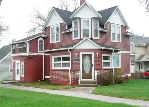 A two-story red house with a unique architectural design, featuring a front porch and a well-maintained lawn.