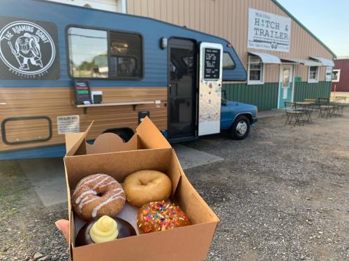A hand holds a box of donuts in front of a food truck named "The Roaming Donut" at a trailer park.