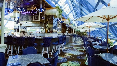 Bright, modern restaurant interior with a bar, blue decor, and large windows showcasing a scenic view.