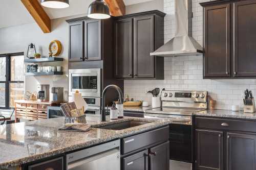 Modern kitchen with dark cabinets, stainless steel appliances, and a granite countertop, featuring a stylish design.