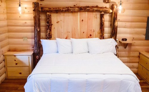 Cozy wooden bedroom featuring a log bed frame, white bedding, and warm wooden walls with soft lighting.