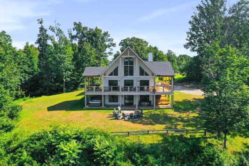 A modern two-story house surrounded by trees, featuring a spacious deck and outdoor seating area.