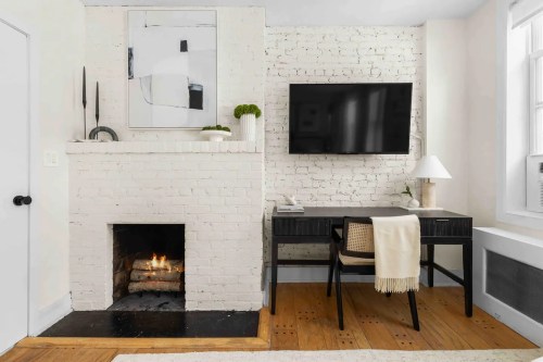Cozy room with a white brick wall, a fireplace, a desk, a TV, and modern decor elements.