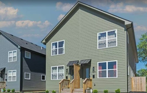 A modern two-story house with green siding, large windows, and a wooden porch, surrounded by a well-maintained yard.