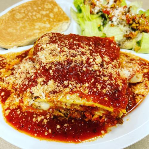 A plate of lasagna topped with marinara sauce and cheese, served with a side of salad and a piece of bread.