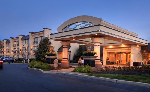 A modern hotel entrance at dusk, featuring a glass canopy and landscaped surroundings.