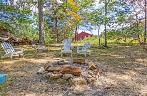 A cozy fire pit surrounded by chairs in a wooded area, with a red barn visible in the background.