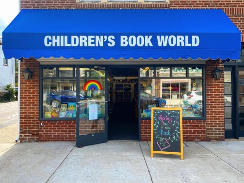 Exterior of Children's Book World with a blue awning, colorful book displays, and a spring-themed chalkboard sign.