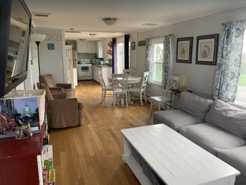 Cozy living area with a sofa, dining table, and kitchen visible in a bright, airy space with wooden floors.
