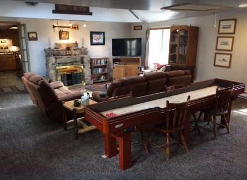 Cozy living room with a stone fireplace, comfortable seating, and a shuffleboard table. Warm, inviting atmosphere.