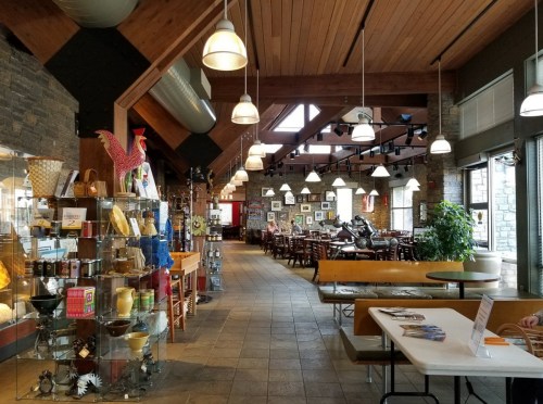 Interior of a cozy restaurant with wooden beams, stone walls, and display cases, featuring tables and chairs in a warm atmosphere.
