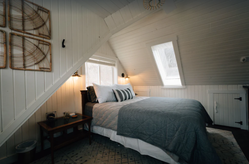 Cozy bedroom with sloped ceiling, featuring a bed, nightstands, and natural light from angled windows.