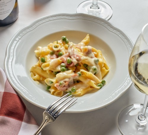 A plate of creamy pasta with peas, served with a glass of white wine and a checkered napkin.