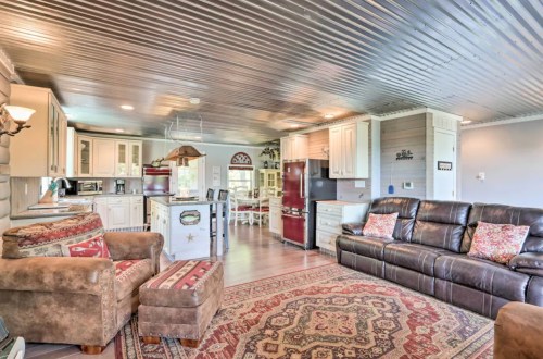 Cozy living area with leather sofas, patterned rug, and open kitchen featuring white cabinets and modern appliances.
