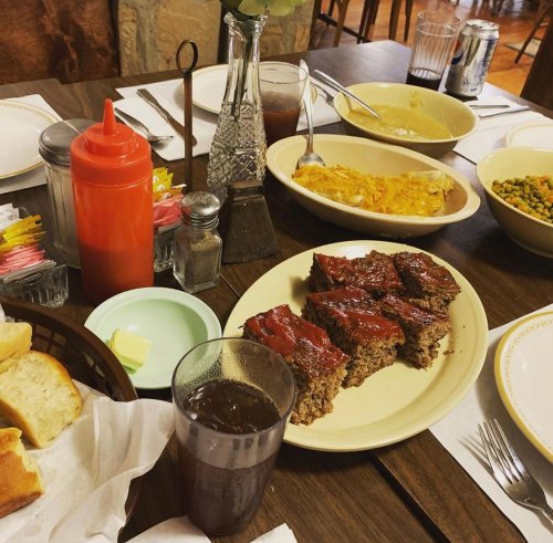 A table set with meatloaf, sides, drinks, and condiments, featuring bread and a cozy dining atmosphere.