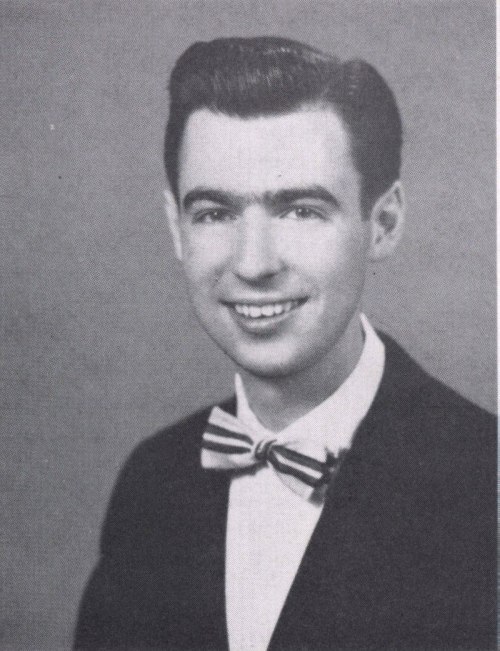 Black and white portrait of a young man in a suit and bow tie, smiling at the camera.