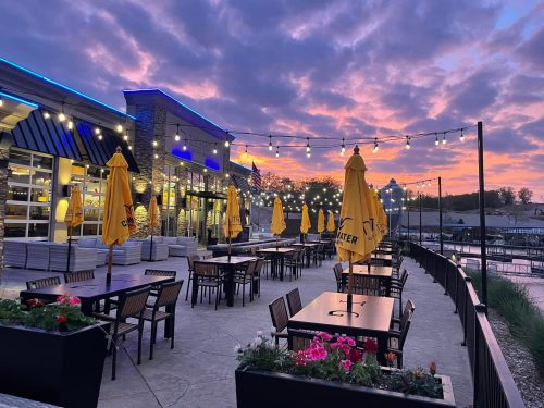 Outdoor dining area with yellow umbrellas, tables, and a colorful sunset sky in the background.