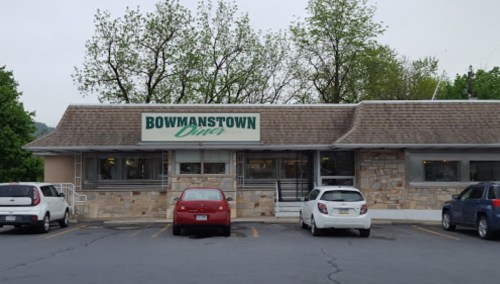 Exterior of Bowmanstown Diner, featuring a stone facade and several parked cars in the lot. Trees in the background.