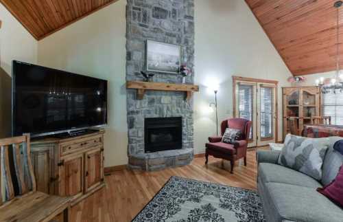 Cozy living room with a stone fireplace, wooden accents, a TV, and comfortable seating. Warm, inviting atmosphere.