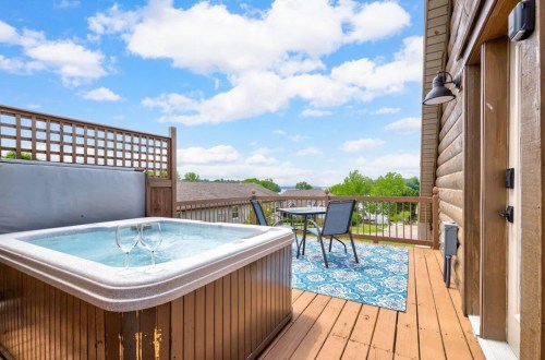 A cozy outdoor deck with a hot tub, two chairs, and a beautiful view under a blue sky with fluffy clouds.