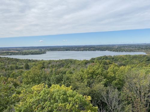 A scenic view of a lake surrounded by lush green trees under a partly cloudy sky.