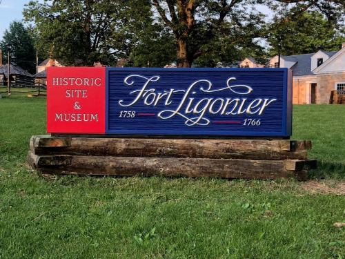 Sign for Fort Ligonier, a historic site and museum, displaying the years 1758 and 1766. Green grass and trees in background.