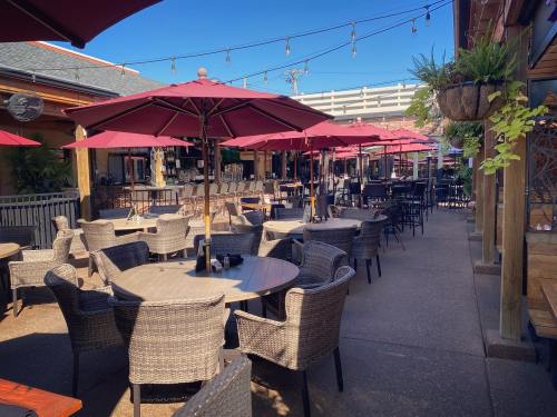 Outdoor dining area with wicker chairs and tables, shaded by red umbrellas, under a clear blue sky.