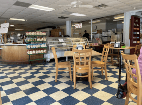 A cozy café interior with checkered flooring, wooden tables, and a display case filled with pastries.