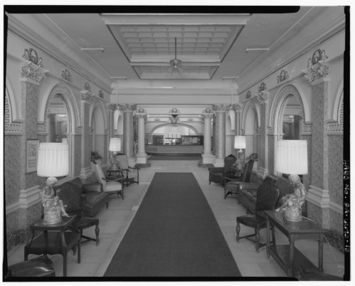 Black and white image of a hotel lobby featuring arched doorways, elegant seating, and decorative lamps.