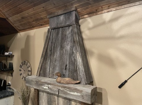 A rustic wooden mantel with a sloped top and a decorative duck figurine on it, set against a neutral wall.