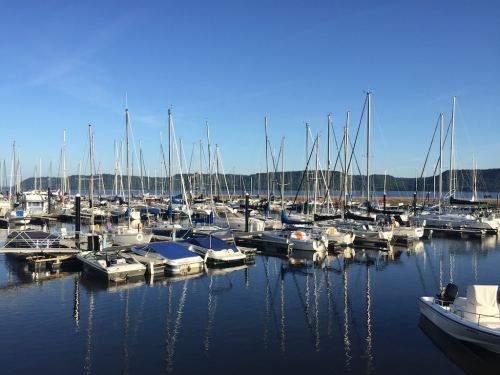 A marina filled with sailboats and yachts, reflecting in calm water under a clear blue sky.