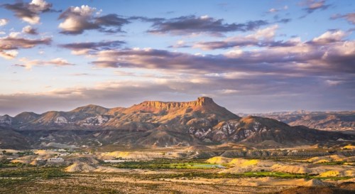 A scenic view of a mountainous landscape under a colorful sky with clouds, showcasing rugged terrain and valleys.