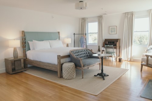 A bright, modern bedroom featuring a large bed, stylish seating, and natural light from windows.