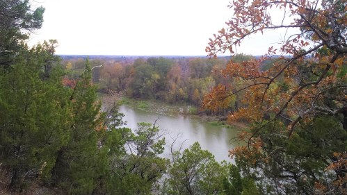 A serene river winds through a landscape of trees with autumn foliage under a cloudy sky.