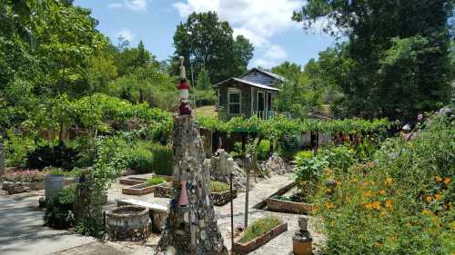 A vibrant garden with stone sculptures, colorful flowers, and a rustic house surrounded by lush greenery under a blue sky.