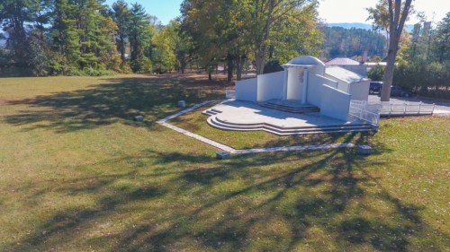 A modern, white structure with steps, surrounded by trees and a grassy area, under a clear blue sky.